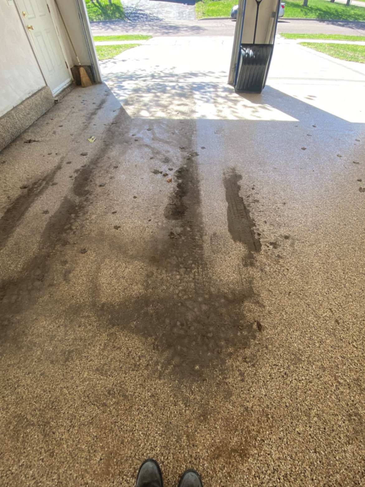Garage floor before pressure washing with dark grime and dirt tracked across the surface
